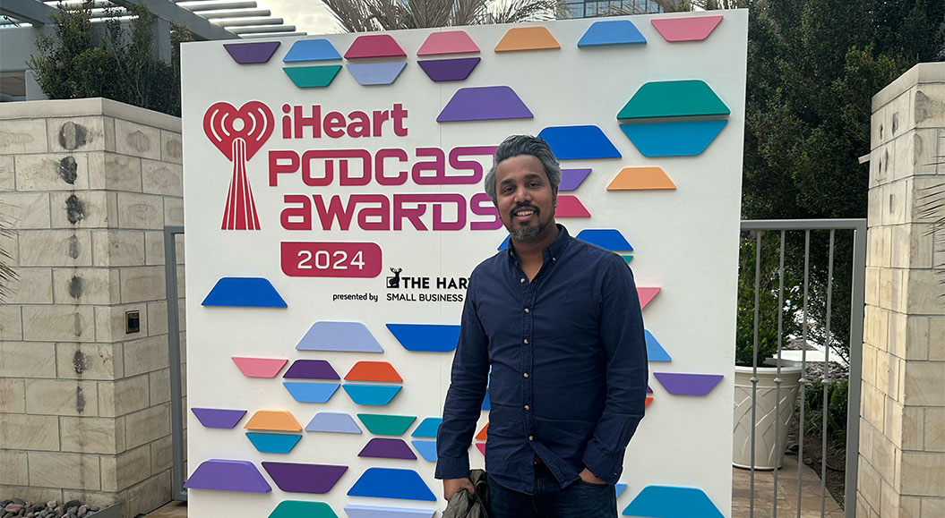 Colin Fernando steht vor einer Fotowand mit dem Schriftzug „Iheart Podcast Awards 2024."