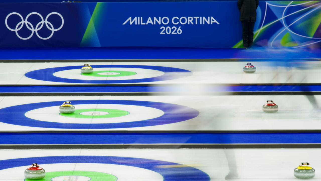 Curling-Bahn bei den Olympischen Winterspielen Milano Cortina 2026 mit spielenden Athlet:innen und sichtbarem Olympia-Branding im Hintergrund.
