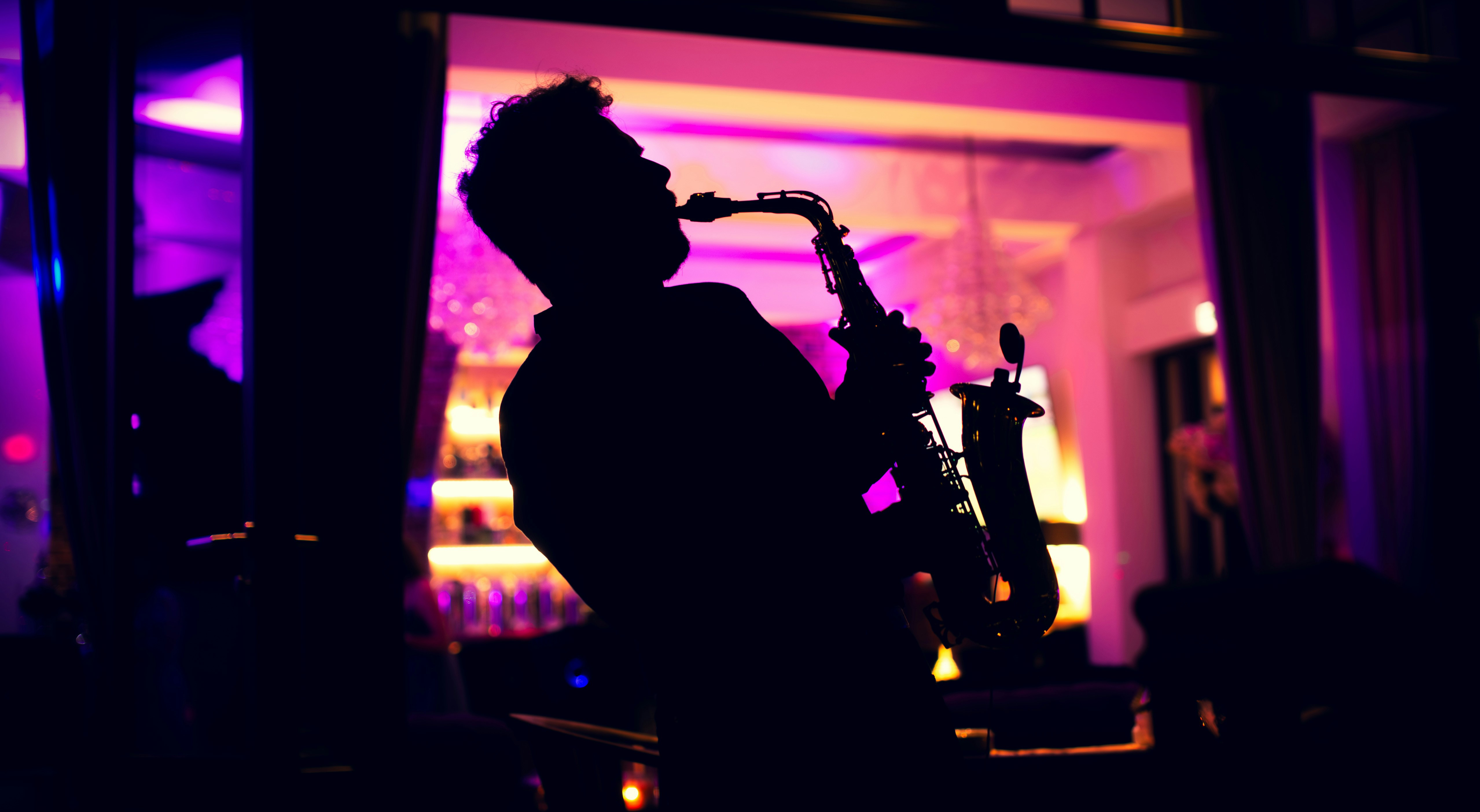 Silhouette eines Saxophonisten vor violett-goldenem Bar-Licht, als Sinnbild für das Zusammenspiel im Jazz-Ensemble